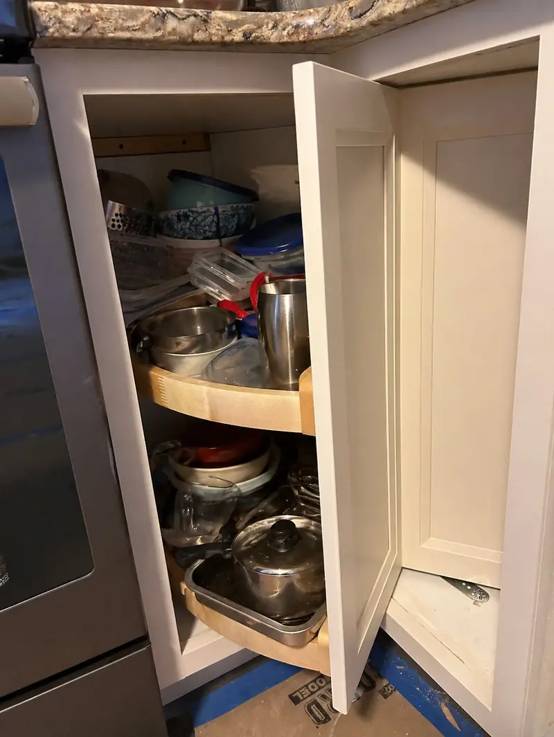 Cluttered corner cabinet with a worn lazy susan before replacement