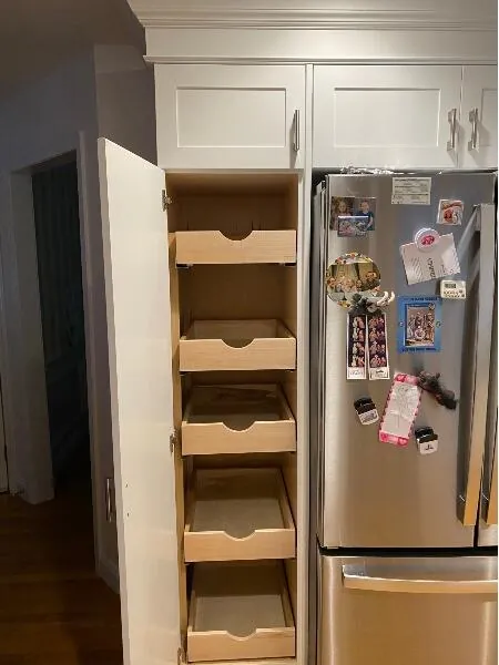 Tall pantry cabinet beside a refrigerator with five wood pull-out drawers